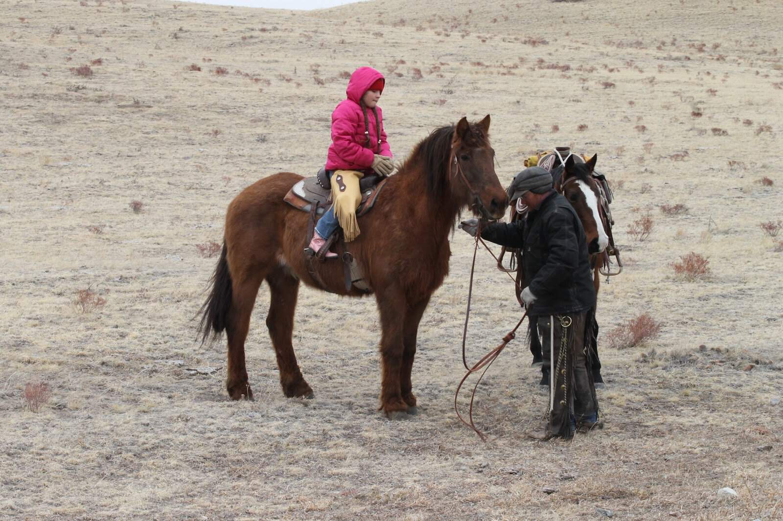 cowgirl in a pink coat on a horse with her dad helping her