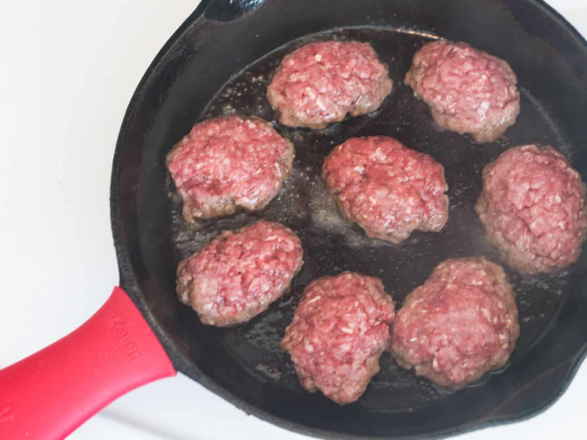 raw beef mini-meatloaves frying in a cast iron pan