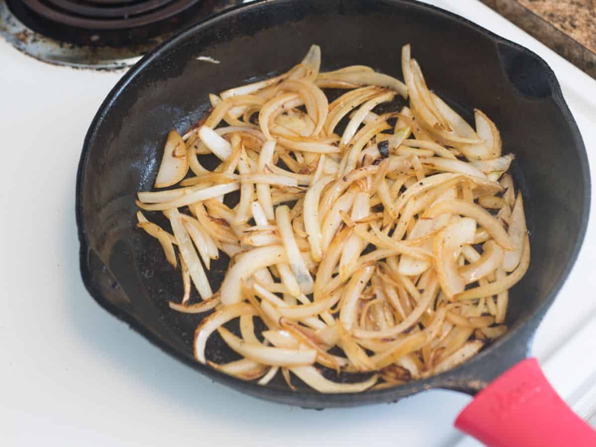sliced onions frying in a cast iron pan