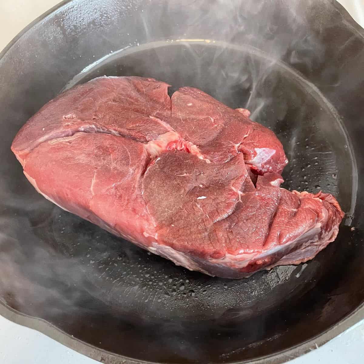 beef roast searing in cast iron skillet