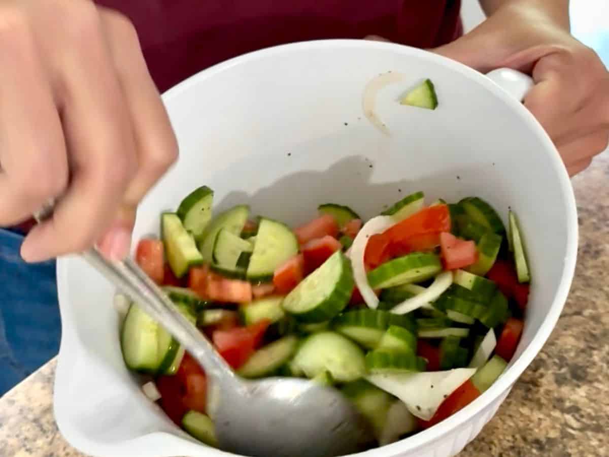 stirring cucumber tomato onion salad with a large spoon.