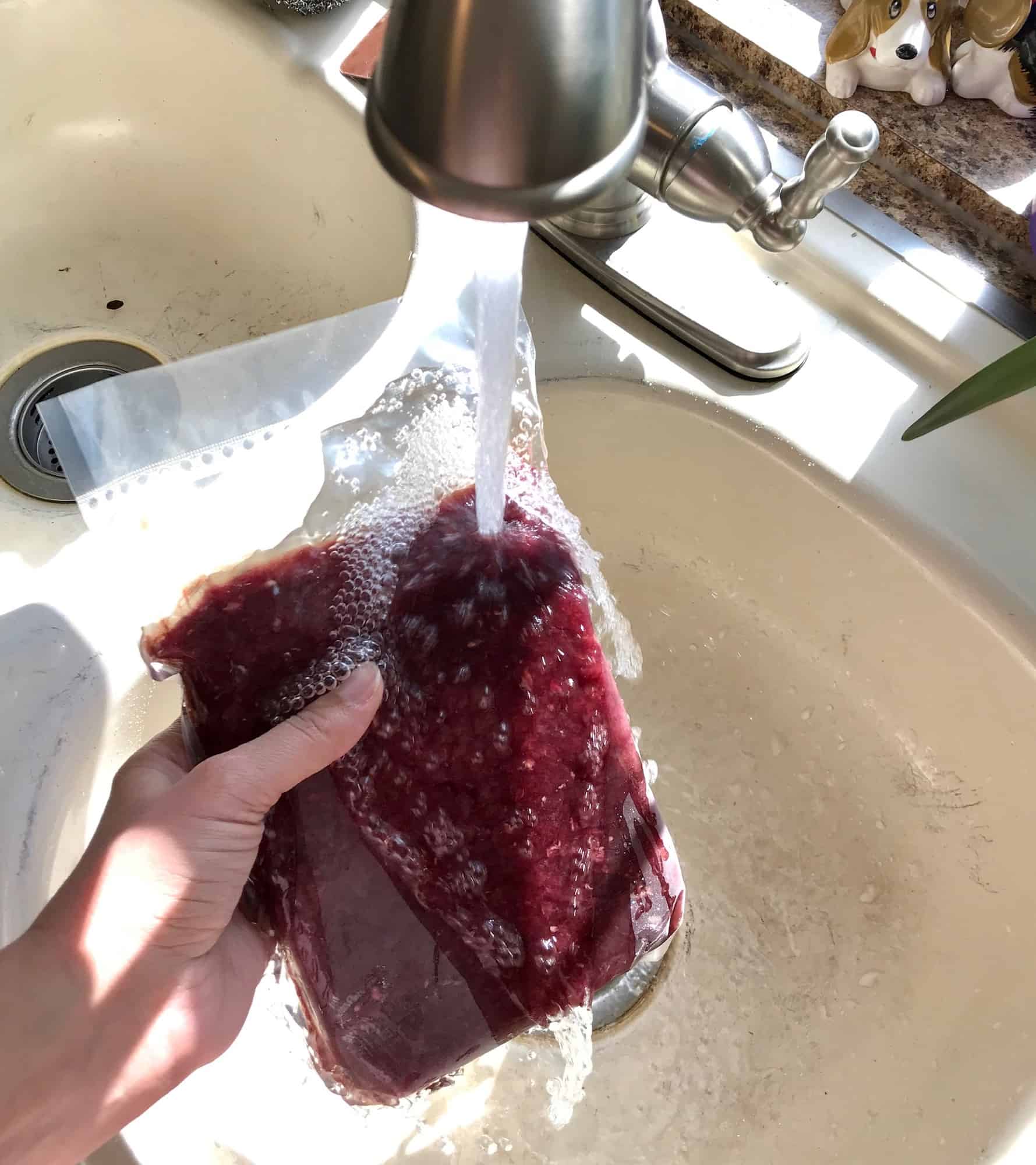 holding frozen meat under running water