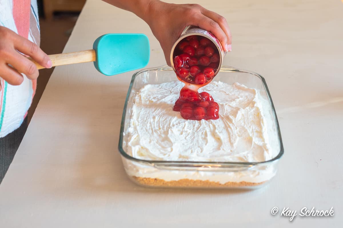 Pouring a can of cherry pie filling over the cheesecake filling
