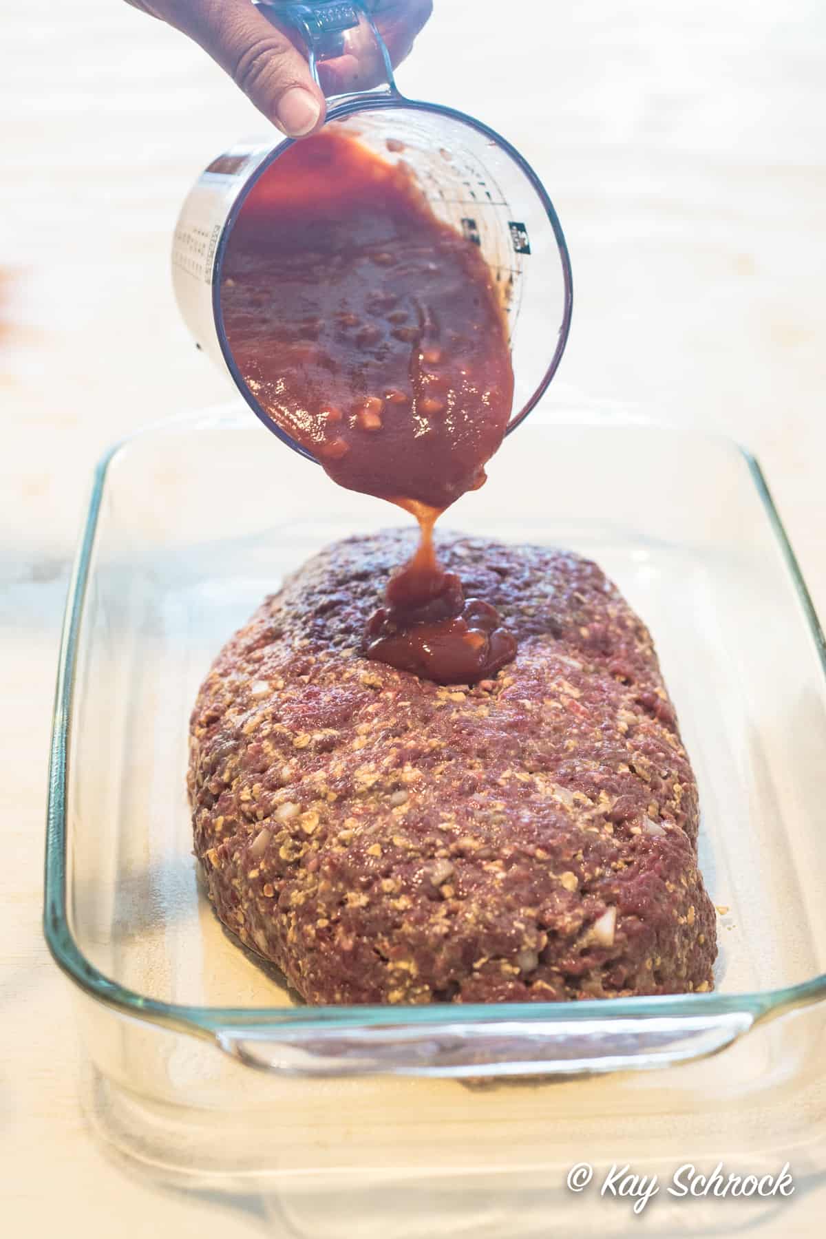 Pouring sauce over unbaked meatloaf