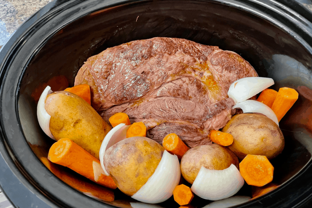 seared beef roast in crockpot with raw vegetables around the side