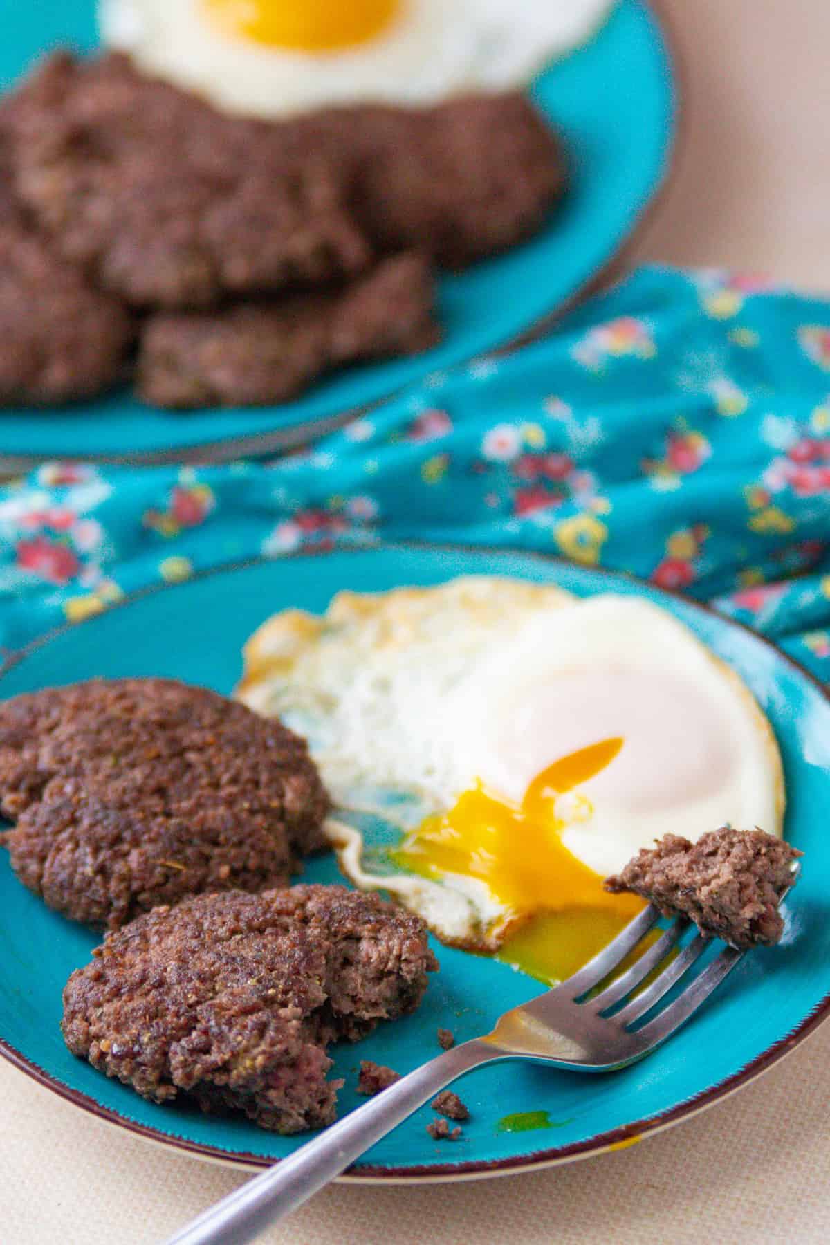 Venison sausage patties and an egg and fork on a blue plate.