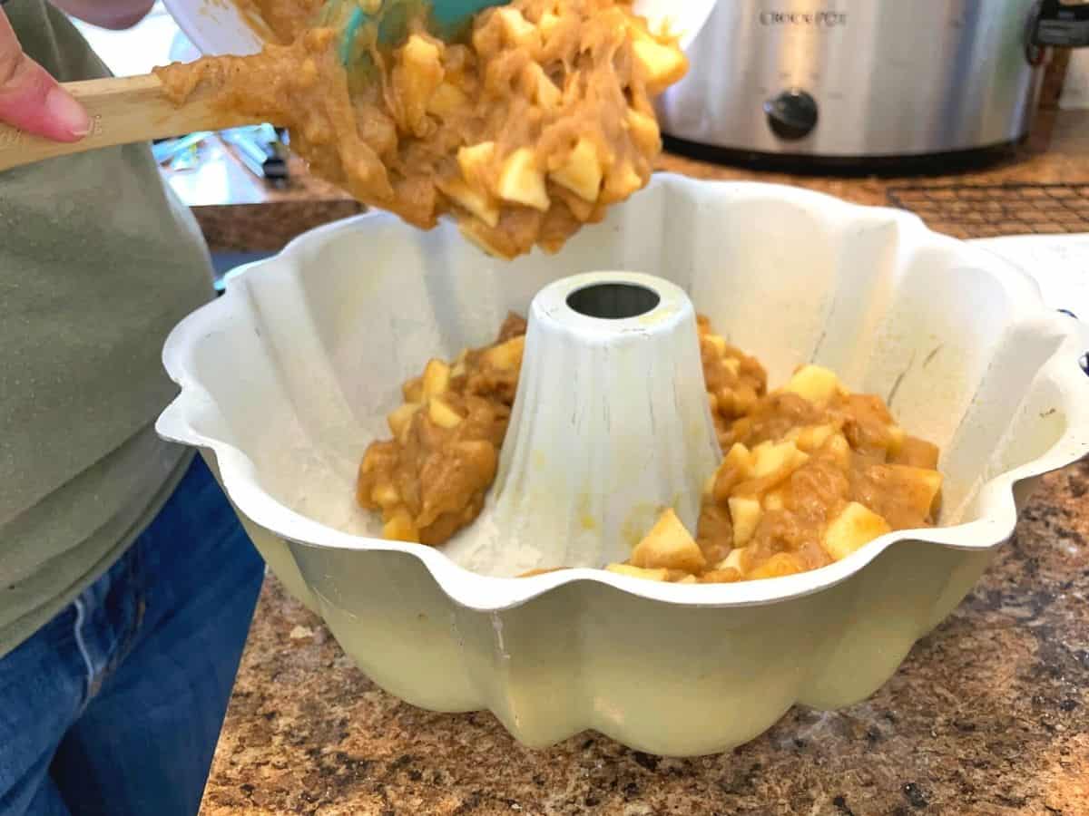pouring apple cake batter into a bundt cake pan