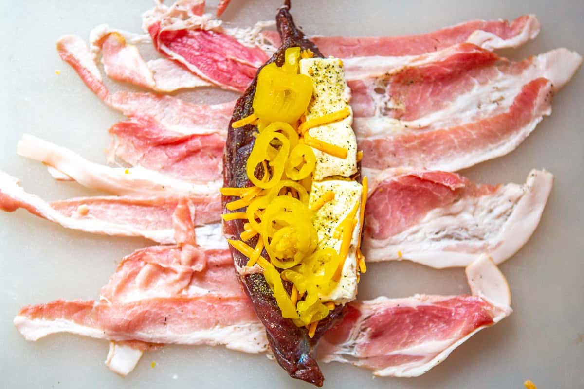 cheese and peppers laying on butterflied venison tenderloin, with bacon.