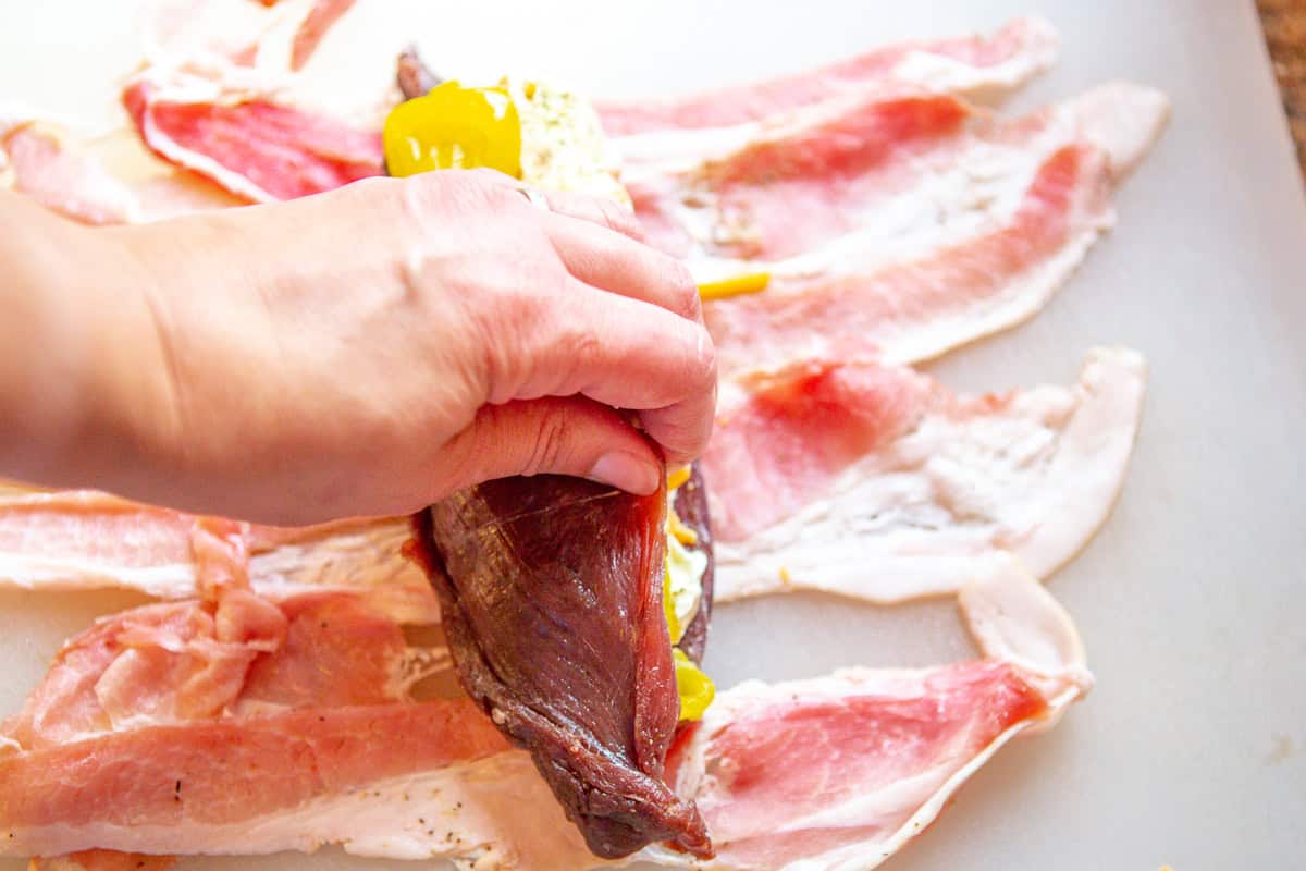 hand holding stuffed tenderloin together while wrapping in bacon.