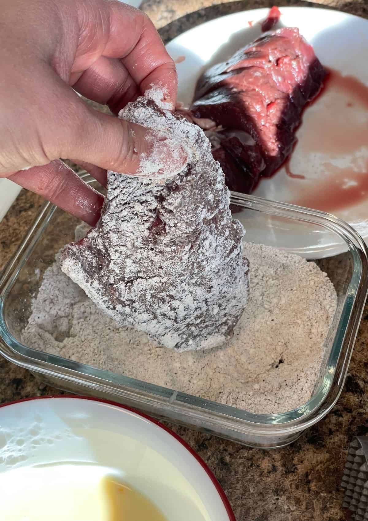 hand dipping deer steaks into flour mixture