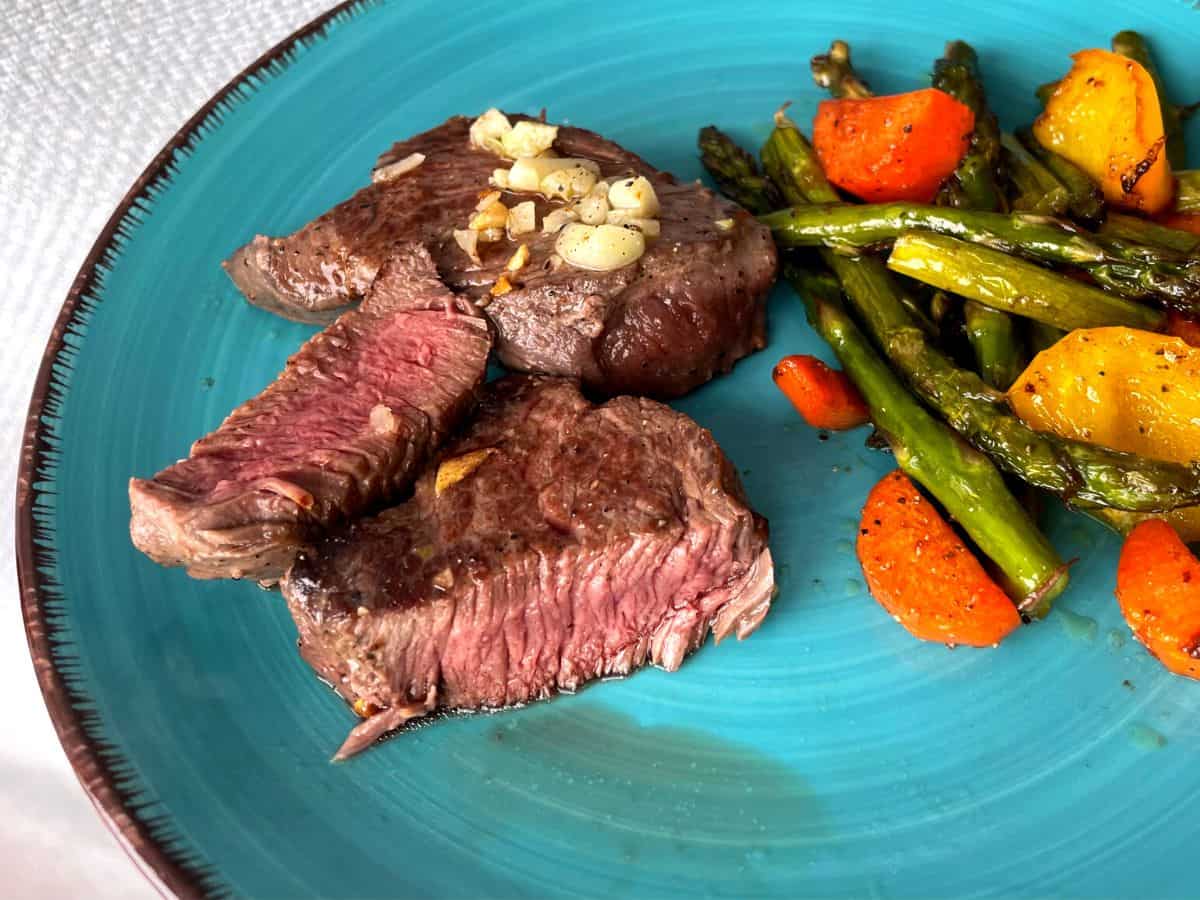 pan seared venison on a blue plate with roasted veggies on the side