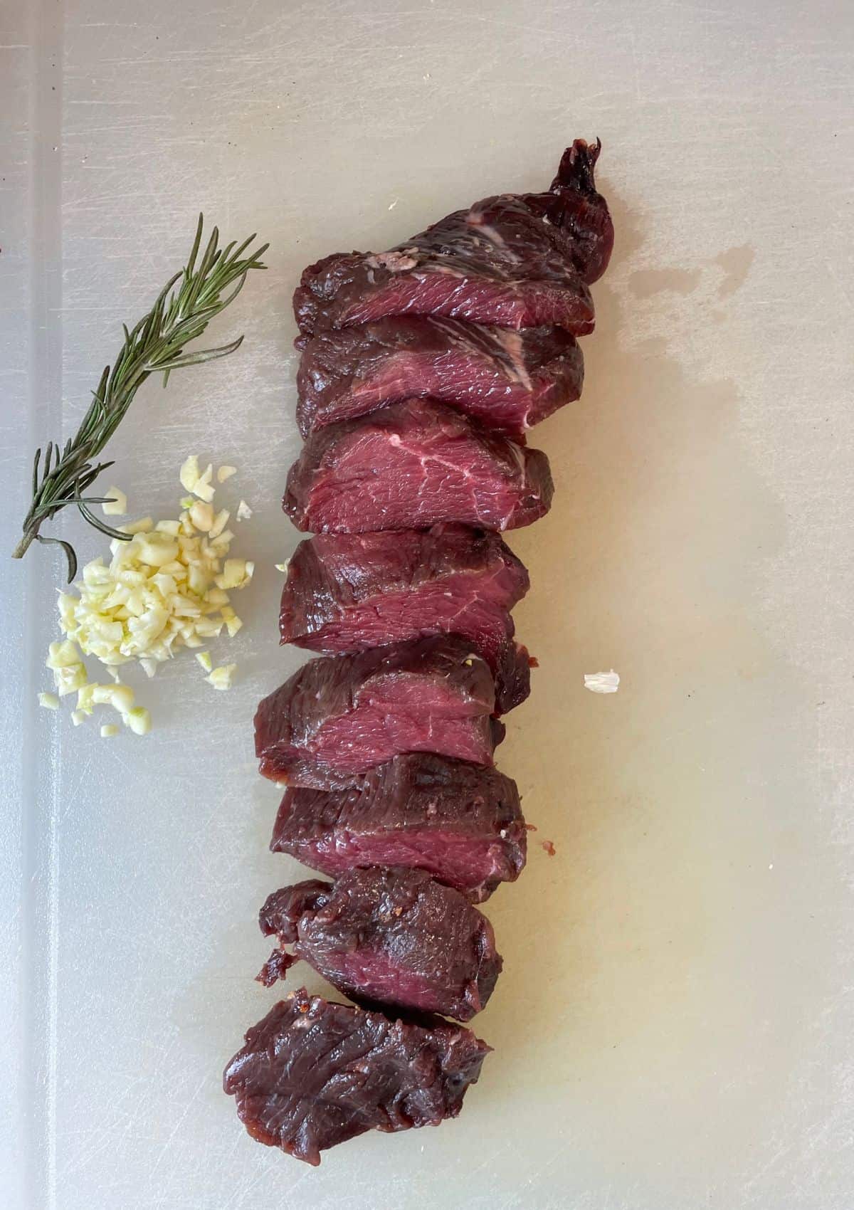 uncooked venison backstrap on cutting board with rosemary and garlic