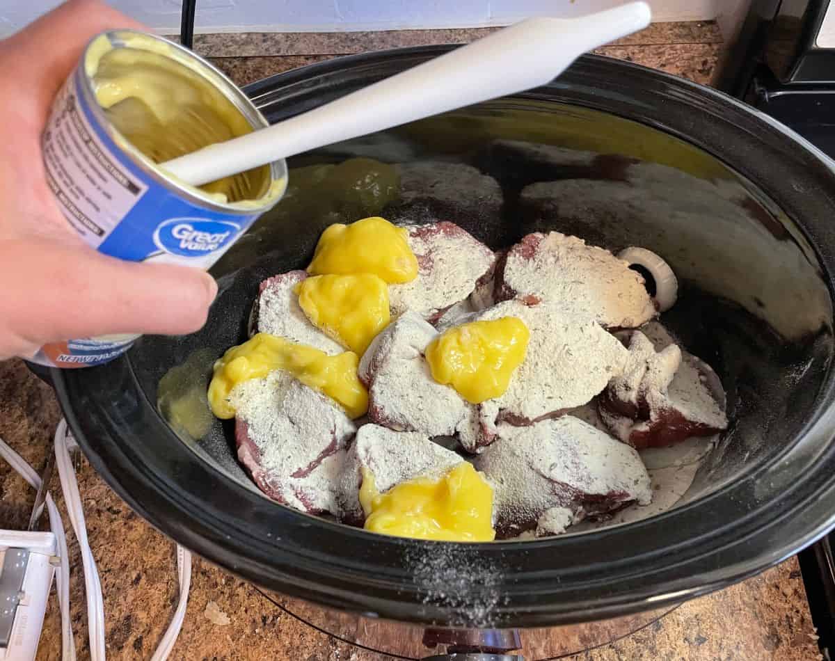 can of cream of chicken soup being spooned over roast in crockpot